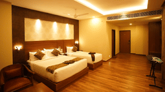 A corner angle of family room with two beds that is king size bed and single bed, several pillows, a chair, a table, wooden floor, ceiling fan, lighting, and an entrance area at V FIVE HOTEL