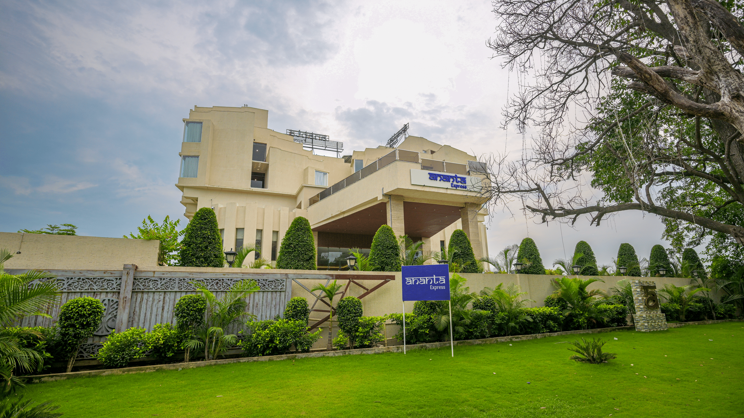 Hotel exterior viewed across a manicured lawn with landscaped shrubs, mature trees and the building entrance in the background.