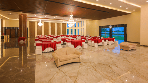 Large banquet hall arranged with round tables, white and red chair covers, decorative lighting and a polished marble floor.