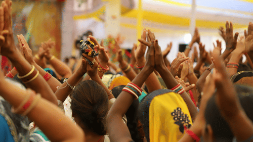 A group of people standing with folded hands, offering prayers to the lord in devotion.