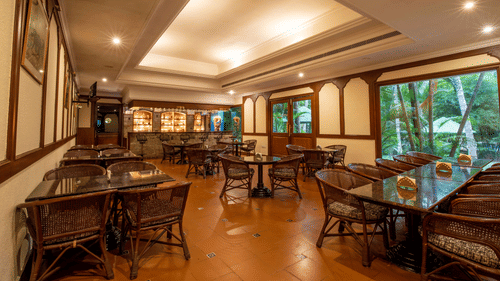A warmly lit indoor restaurant and bar in Coimbatore featuring seating with wicker chairs, large windows, warm ambience, and scenic outdoor views at Black Thunder.