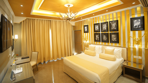 An Executive Suite bedroom at Clarks Khajuraho with a bed, a patterned accent wall with framed artwork, ceiling lighting, and curtains covering a large window.