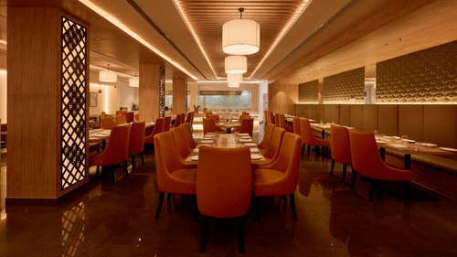An image of our restaurant with orange chairs placed around tables under chandeliers 