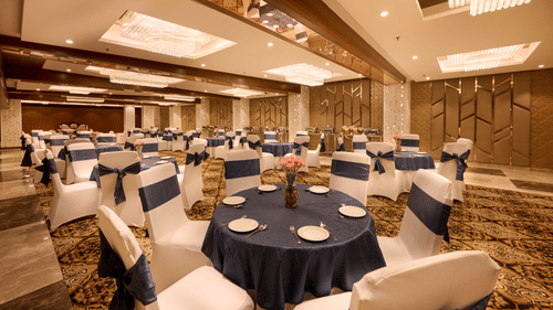 A banquet hall with round tables covered in blue cloth and chairs around it