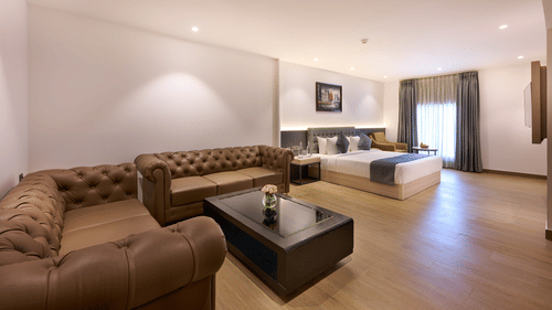 A hotel suite with a sofa beside a bed and a window providing light