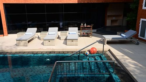 The outdoor swimming pool area with lounging chairs placed besides it at Golden Tulip Vagator, Goa