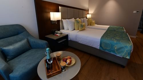 A room at Golden Tulip Vagator, Goa with twin beds, a sofa chair and a coffee table set up