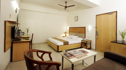 Suite room with a comfortable bed, seating area, table and wooden furnishings at Hotel Geetha Regency, Guntur.