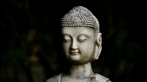 Serene stone Buddha statue with a peaceful expression against a dark, blurred background.