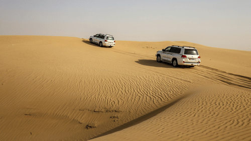 Two SUVs driving through the dunes in a desert on a clear day