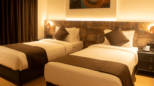 2 single beds room with bedside lamps, headboard panel, and wall art at Magnus Lxia Premier, Kalyani Nagar.