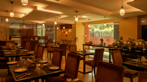 Amara restaurant featuring chairs and tables which have plates, cutlery, glass and napkin. The area is lit with dim lights which are hanging from the ceiling.