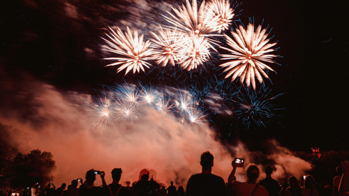A large cluster of white and gold fireworks exploding above a crowd of people watching in the dark.