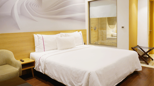 Deluxe room at Nemesia with a king size bed, modern decor, and a stylish en-suite bathroom visible through a glass partition.