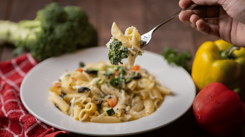 Image of a plate of pasta with vegetables on the side of the plate at Pride Elite Daman.