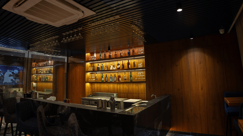 Image of a bar with wooden decor and drinks stacked in the shelf at Pride Elite Daman.