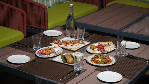A beautifully set outdoor table at Pride Elite Himmatnagar showcases a selection of delicious appetizers.
