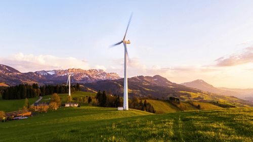 An image of a windmill farm with greenery around
