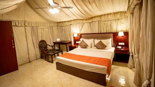 Cottage at Pride Hotel and Convention Centre, Indore featuring a plush bed with two nightstands on both sides and lamps mounted on them and a sitting space next to it