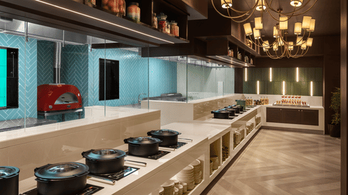 A restaurant kitchen with light blue walls, a white stone countertop, and a red oven at Sarovar Portico, Hanumangarh.