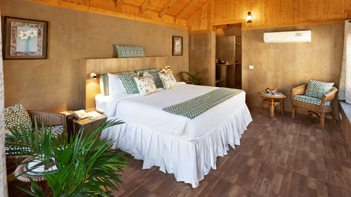 An attic style bedroom featuring double size bed, a bedside table, flower pots, and a seating area at Suryavilas Luxury Resort and Spa