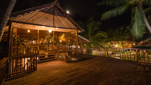 exterior of Venom Bar at night surrounded by palm and coconut trees and decorated by soft yellow lights - Symphony Palms Beach Resort And Spa