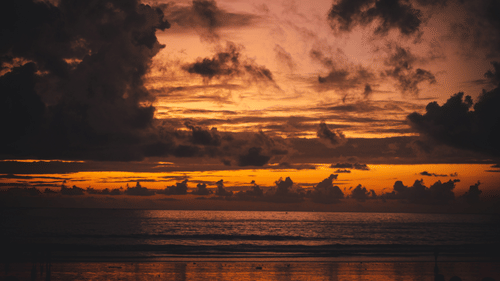 A sunset over waters at a beach with coloured clouds along the horizon.