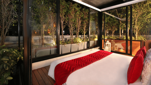 A bedroom at Theory9 - Premium Service Apartments, Bandra with a large bed and floor-to-ceiling windows overlooking a night-time rooftop garden with trees