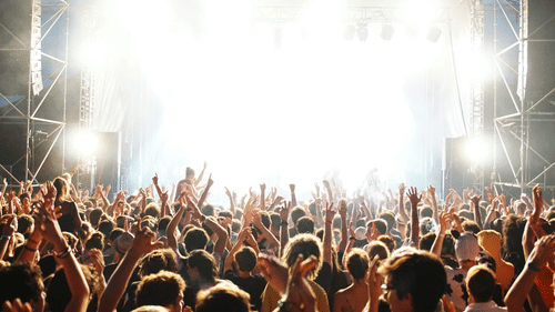 Large festival crowd cheering in front of an intensely lit stage.
