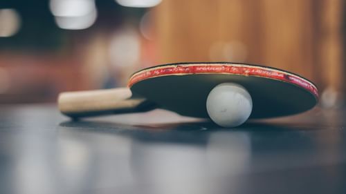 A close-up shot of a table tennis paddle resting on a glossy surface with a white ball placed under the paddle