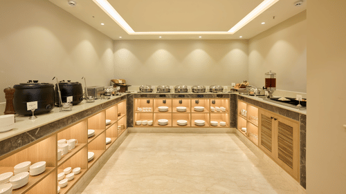 A buffet area at Tulip Inn Gurugram showing warm wooden counters with food warmers and dishware beneath soft lighting.