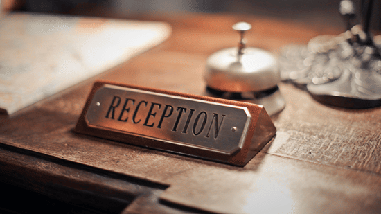 Wooden reception desk sign placed beside a service bell at a hotel reception counter.