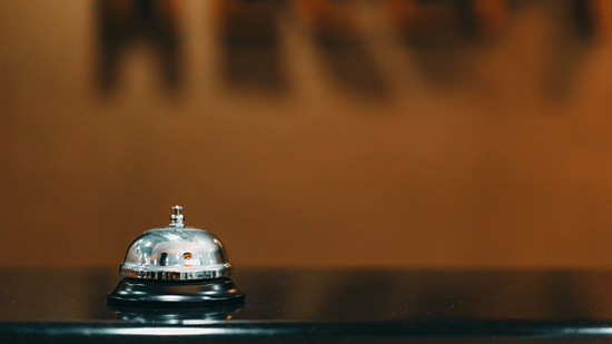 Silver service bell placed on a wooden hotel reception counter.