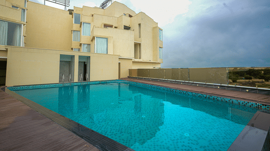 Outdoor swimming pool beside the hotel building, with a tiled deck and open view towards the surrounding landscape.