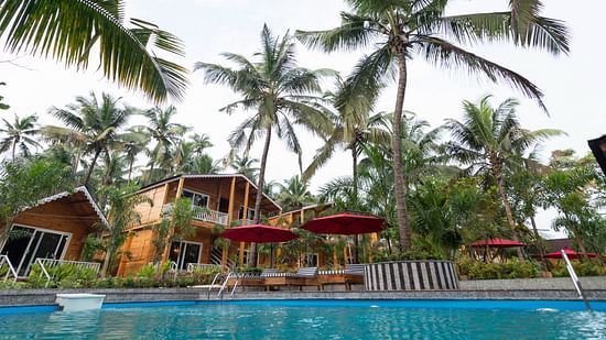 A resort swimming pool with red umbrellas, wooden loungers, surrounded by tropical vegetation and wooden cabins Aralea Beach Resort by Stone Wood, Morjim