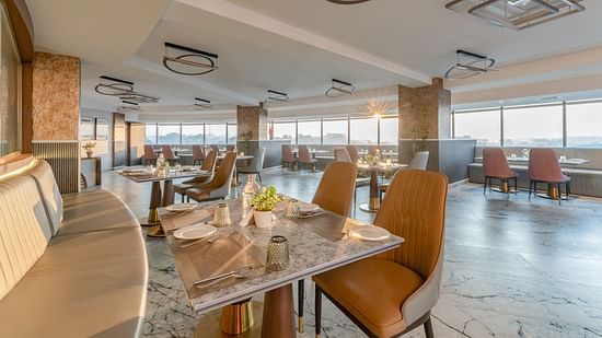 Cosy dining setup with curved banquette seating, marble tables, leather chairs and decorative ceiling lights at Clarks Inn Suites, Hyderabad