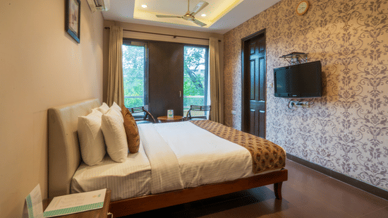 Room at Cosy Grand @Chanakyapuri by The Cosy Hotels with double bed, balcony view, and flat-screen TV.