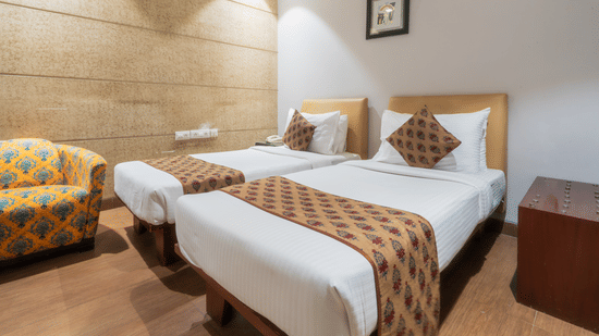 A room at Cosy Grand at Chanakyapuri By The Cosy Hotels featuring two similar looking beds, a bedside table, and a sofa chair.