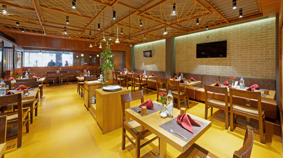 A modern restaurant at Icon Boutique Hotel by Bhagini, Domlur, with wooden furniture, a brick wall, and a view of the kitchen.