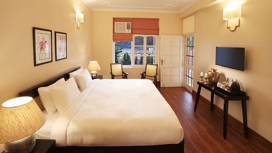An image of a Super Deluxe Room equipped with soft bedding, modern furniture, flat TV screen, and a seating area with chairs  - Lamrin Boutique Cottages Rishikesh