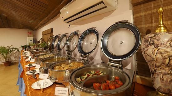 A buffet setup with a variety of dishes presented in metal containers, ready for service, in a dining room with warm lighting- Lotus Eco Beach Resort, Konark.