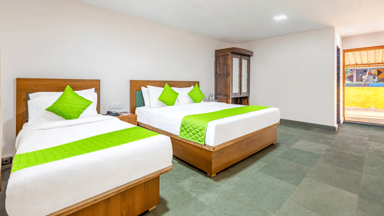 Family room at Nature Trails Durshet with two beds, green accent pillows, wooden wardrobe, and a sunlit balcony view.
