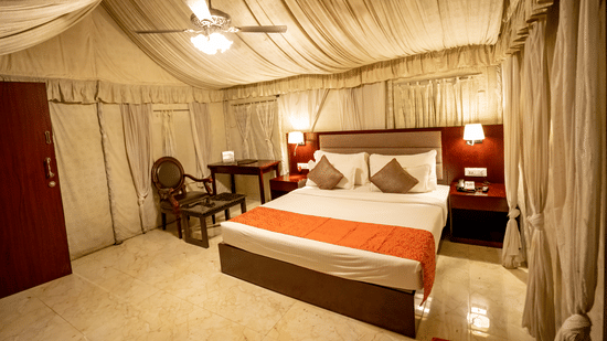 Cottage Room at Pride Hotel and Convention Centre, Indore featuring a plush bed with two nightstands on both sides and lamps mounted on them and a sitting space next to it