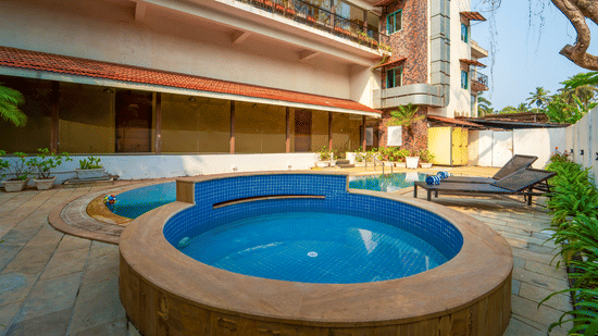 Rosetum Anjuna's circular children's pool with blue mosaic tiles in the foreground, the main swimming pool behind, sun loungers with towels, and the hotel facade in the background.