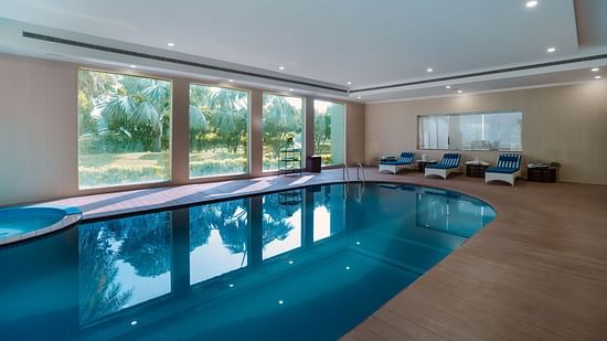Relaxing swimming pool surrounded by large windows with a view of a garden.