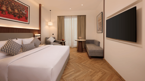 Skywings Sarovar Portico Mathura premium room with king bed, red framed wall art, herringbone wood flooring, pendant lights, and warm interiors.