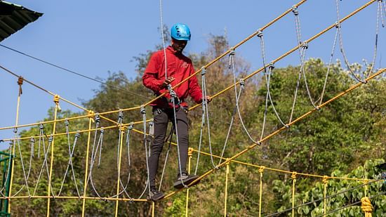 Participant walking on a suspended rope bridge as part of an adventure activity. | Stone Wood Jungle Resort, Dandeli