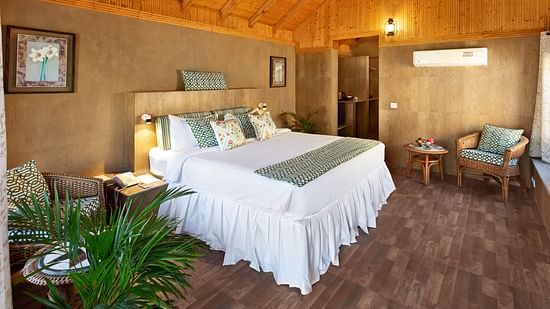 An image of an attic style bedroom featuring double size bed, a bedside table, flower pots, and a seating area at Suryavilas Luxury Resort & Spa, Kasauli