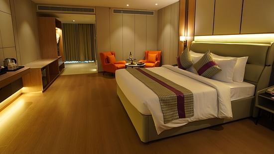 A well-appointed hotel premier room displays a king-sized bed with a striped runner, a seating area with orange chairs, and warm ambient lighting - The Orchid Hotel, Chandigarh
