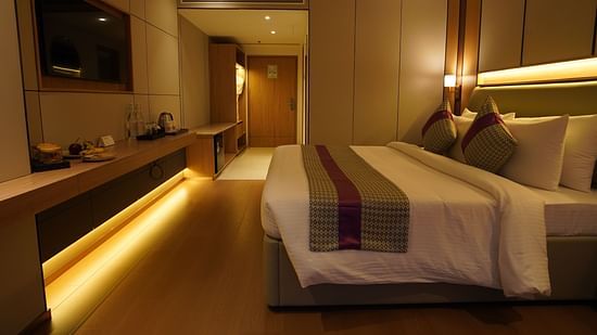 Well-lit Club Room bedroom showcasing a neatly made bed with striped accents, a long work desk with a television, and soft ambient lighting - The Orchid Hotel, Chandigarh